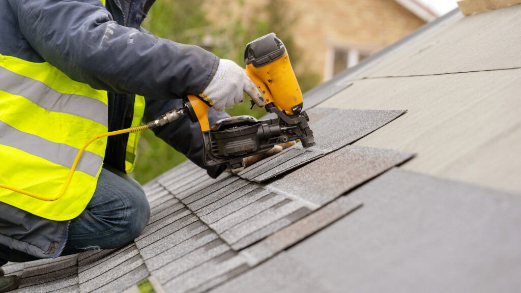 Roofer installing shingles with a nail gun